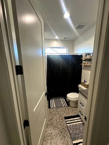 Bathroom featuring tile flooring, a white vanity with dark countertop, a toilet, a shower with a dark curtain, and a horizontal window