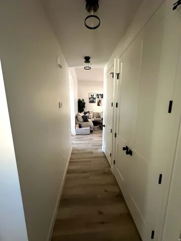 Hallway featuring wood-finish flooring, white walls, and contemporary black ceiling lights