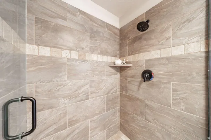 Shower enclosure featuring floor-to-ceiling large format tile, decorative accent band, built-in corner shelf, and matte black fixtures