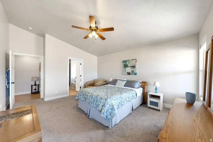Carpeted room with a vaulted ceiling, ceiling fan, natural light, and two doorways