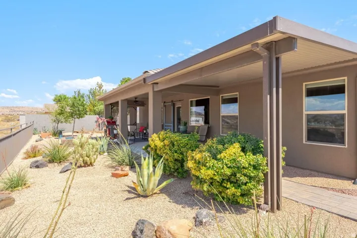 Expansive covered patio with recessed lighting and a ceiling fan, featuring a stone paver walkway and desert landscaping with various succulents, shrubs, and gravel ground cover