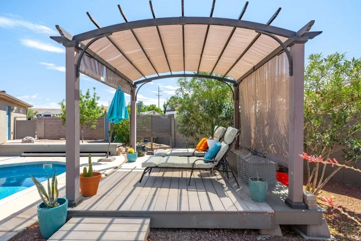 Outdoor living area featuring a covered pergola with retractable shade, composite decking, and a built-in swimming pool with a surrounding hardscape