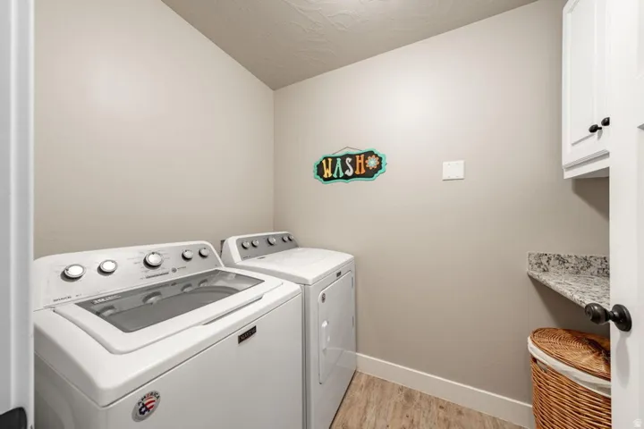 Dedicated laundry space featuring neutral walls, wood-finish flooring, white cabinetry, and a granite-look countertop