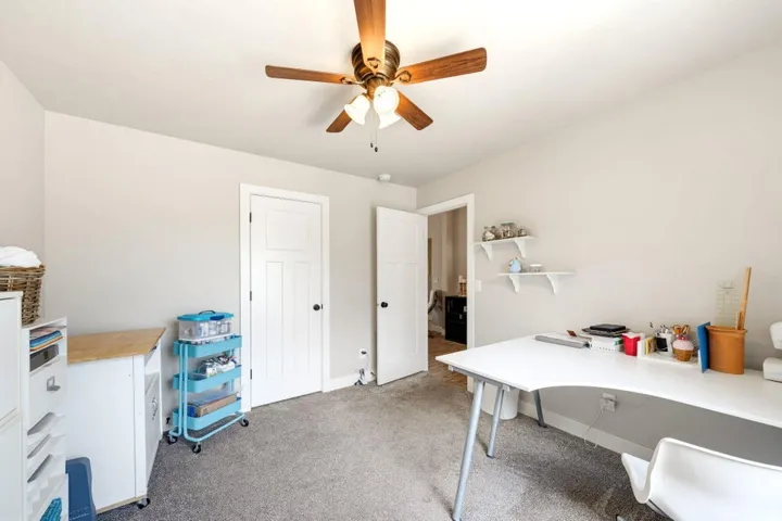 Light gray wall paint with white trim, wood-finish ceiling fan, and gray carpet