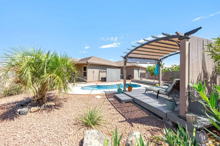 Expansive backyard featuring a built-in swimming pool, a shaded pergola with a deck, and low-maintenance landscaping with rock ground cover and mature palm trees