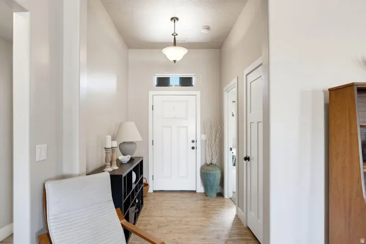 Entryway featuring a white paneled door with transom window, suspended ceiling light fixture, wood-finish flooring, and light-toned walls
