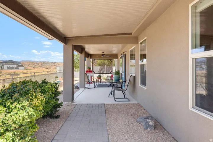 Covered patio featuring an outdoor ceiling fan, stucco exterior, and a paved walkway