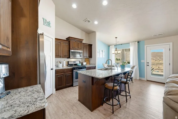 Open-concept kitchen featuring wood-finish flooring, dark wood cabinetry, granite-style countertops, stainless steel appliances, and an island with bar seating