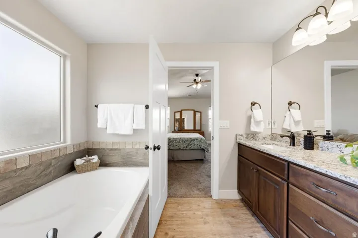 Bathroom featuring a built-in tub with tile surround, a large privacy window, and a dual vanity with a light-toned countertop and dark wood-finish cabinetry
