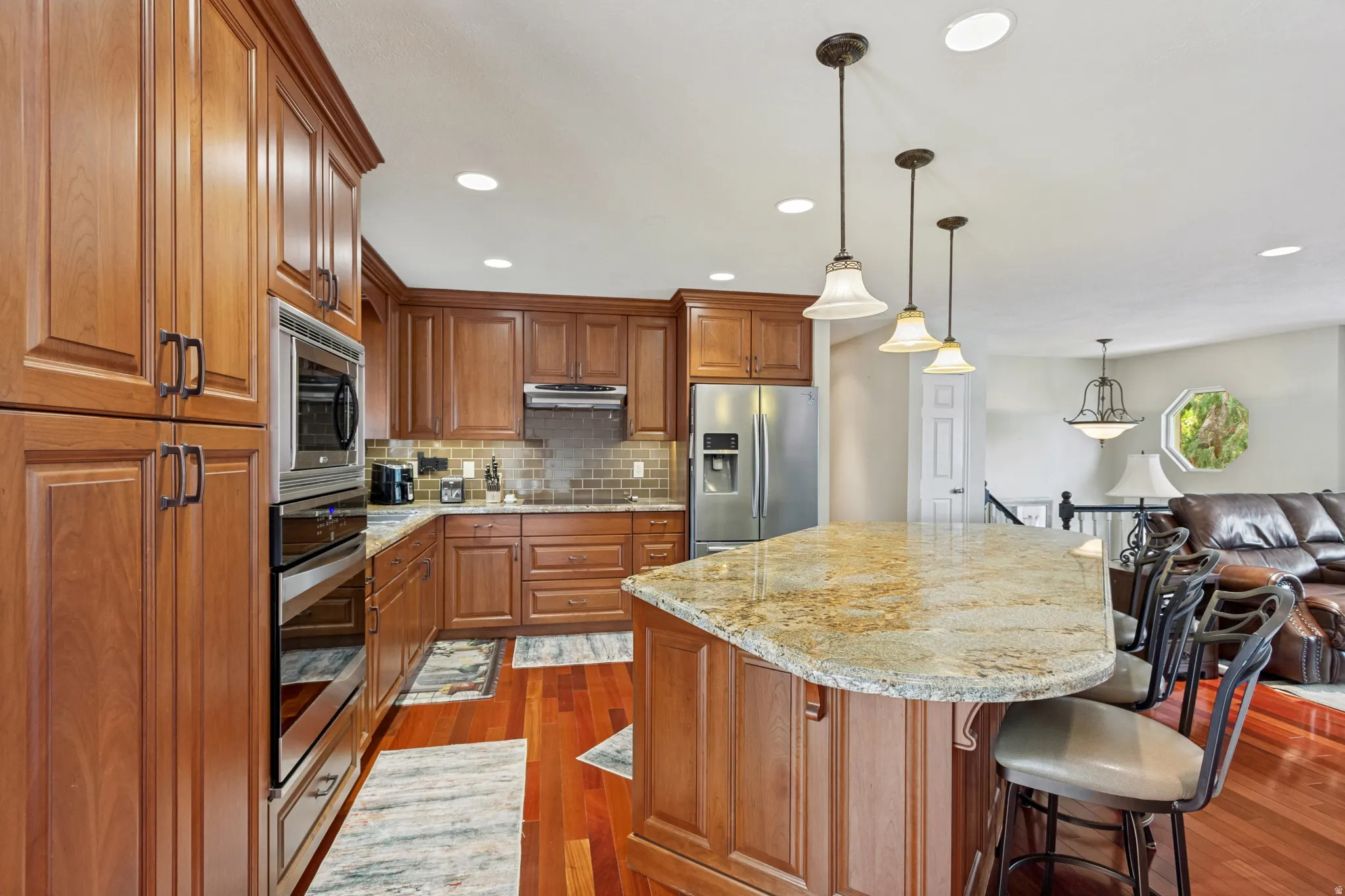Spacious kitchen featuring rich wood cabinetry, stainless steel appliances, a tile backsplash, and wood-finish flooring