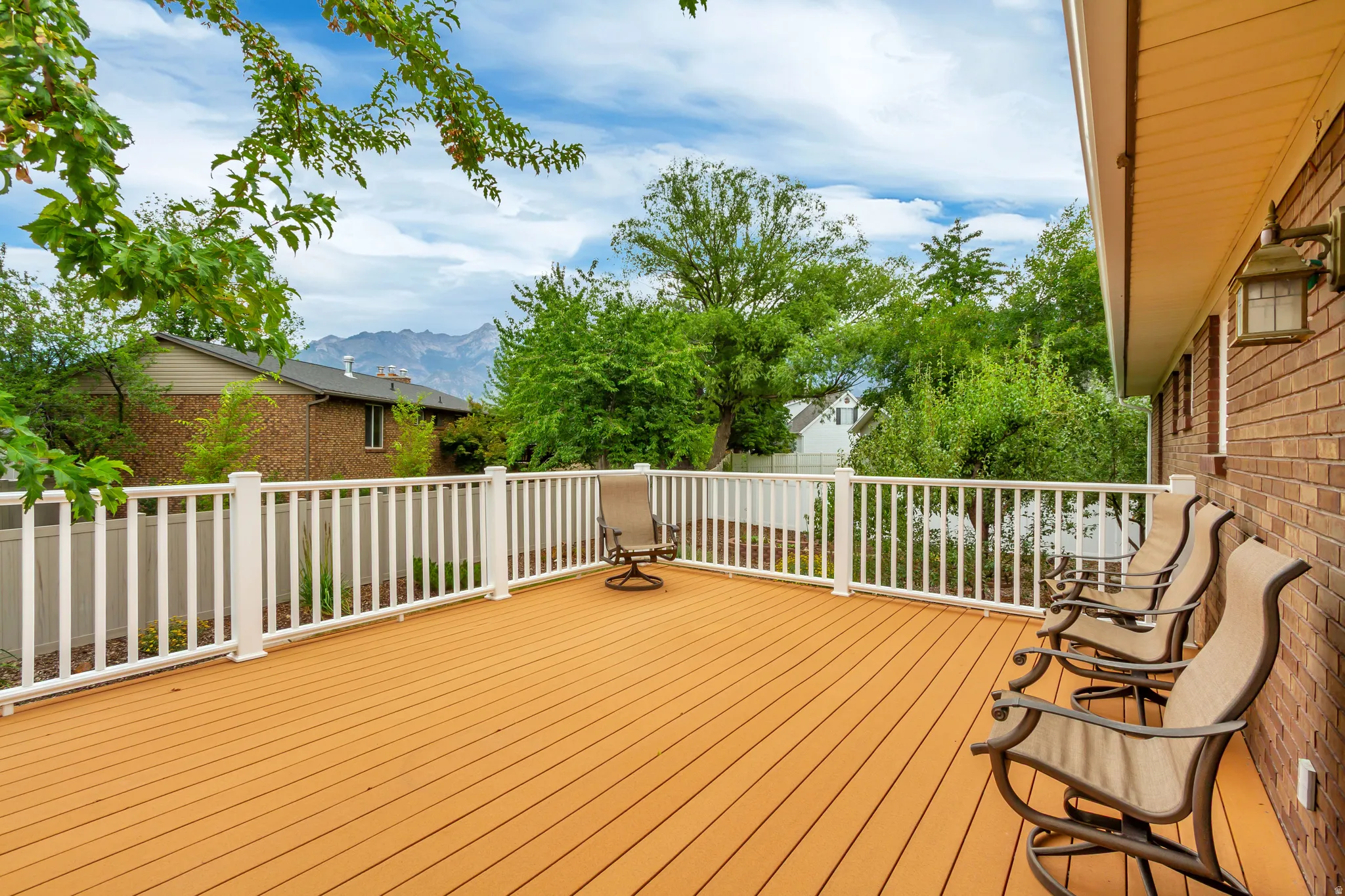 Expansive outdoor deck featuring wood-finish flooring, white railing, and a brick exterior facade