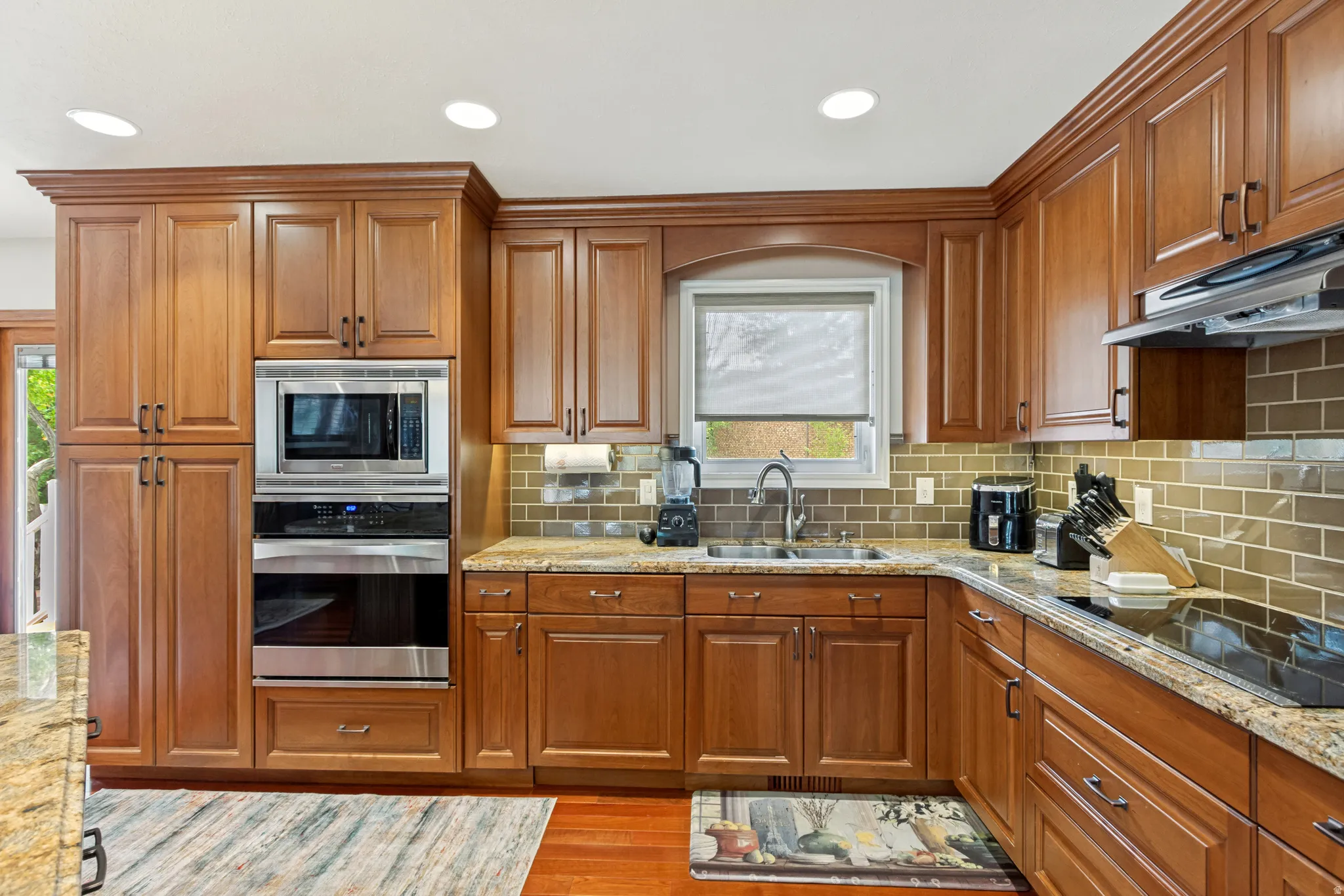 Kitchen featuring wood-finish cabinetry, built-in stainless steel appliances, recessed lighting, a window over the sink, and a tile backsplash