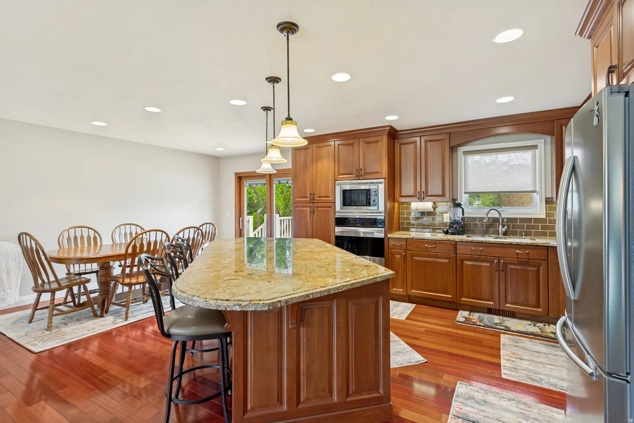 Kitchen featuring a large central island with seating, stainless steel appliances, wood cabinetry, and a tile backsplash