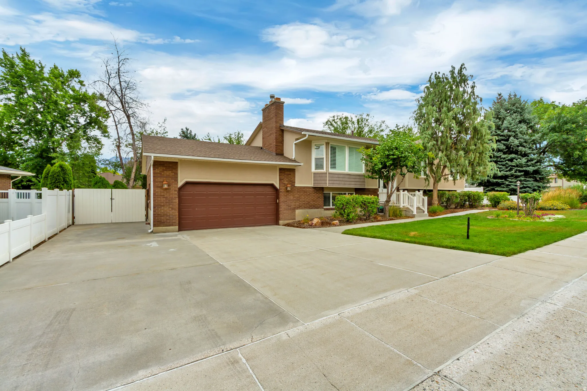 Front exterior featuring a two-car garage with a brown door, brick accents, and a large concrete driveway