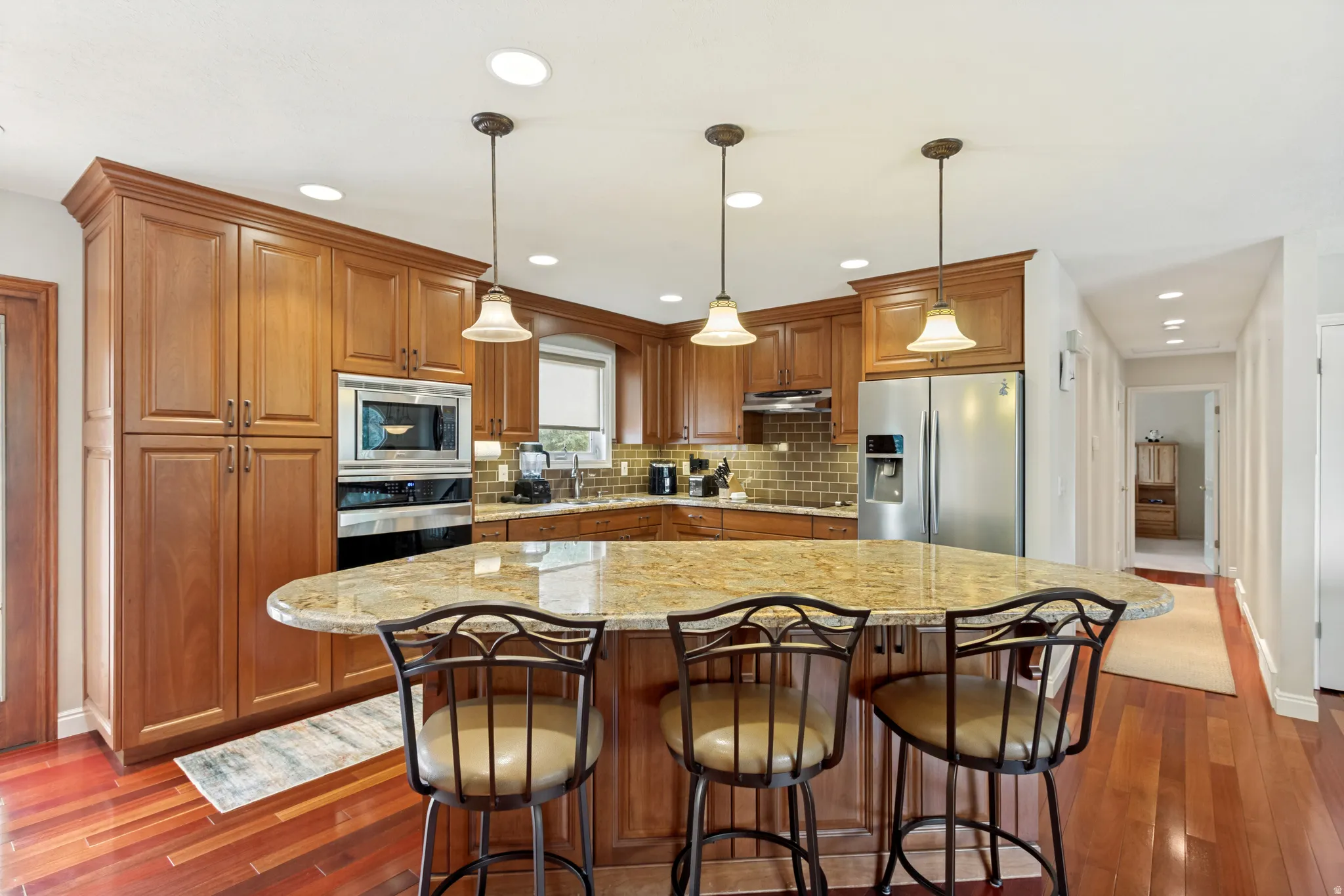 Kitchen featuring wood-finish flooring, an oversized island with a stone countertop, recessed lighting, and pendant lighting