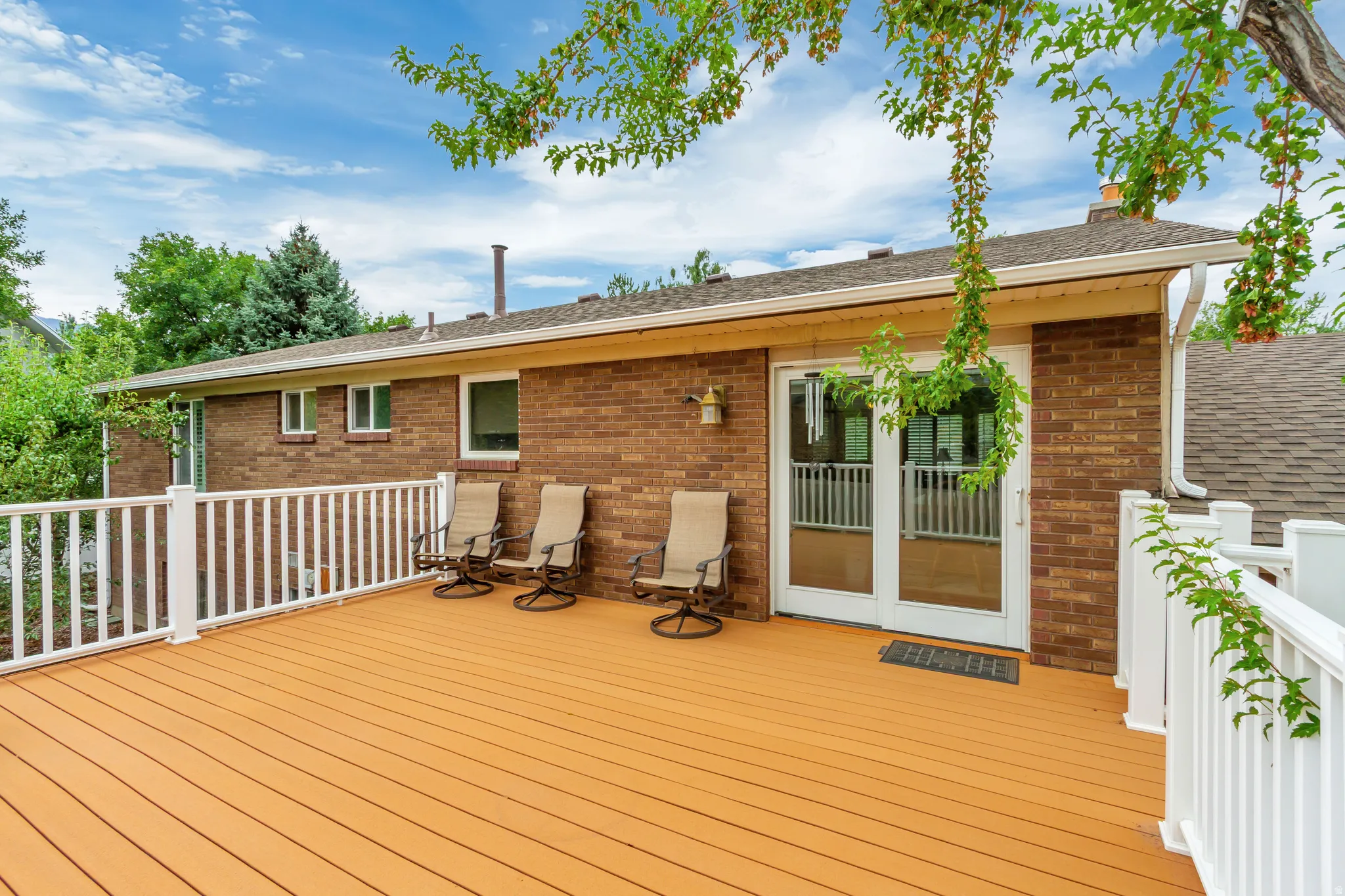 Expansive exterior deck featuring a warm-toned surface, white railing, and direct access to the interior via double glass doors