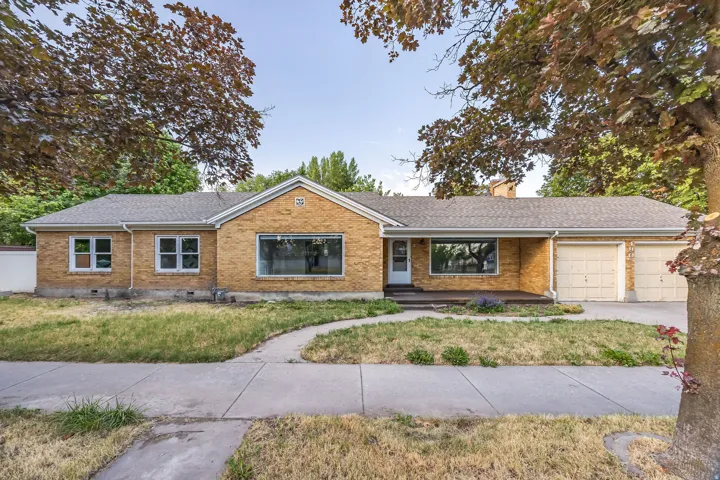 Brick exterior residence featuring a front yard, sidewalk, and mature trees