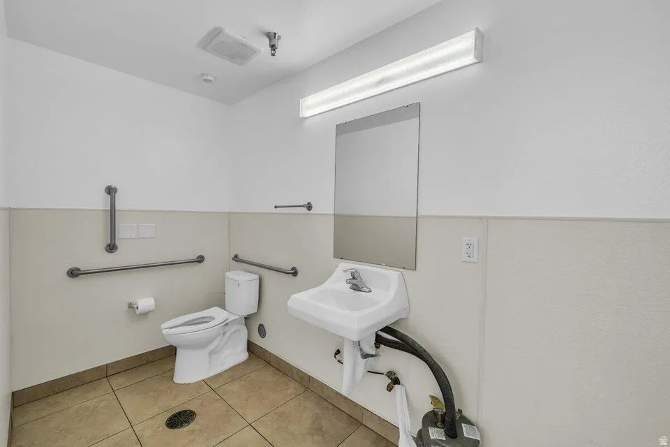 Restroom featuring white walls with a light-colored wainscoting, a wall-mounted sink, and a rectangular mirror