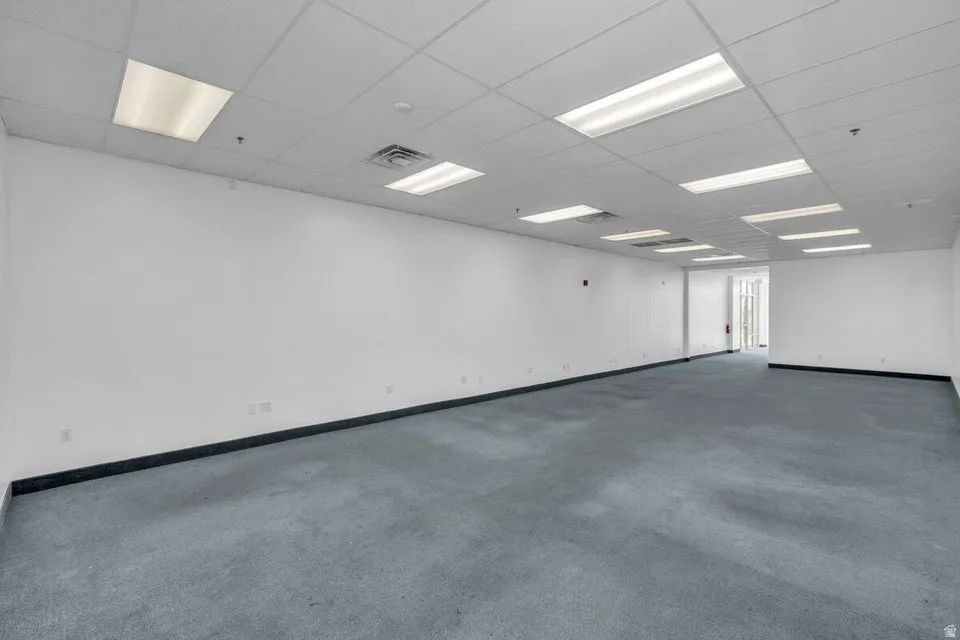 Spacious interior featuring a neutral color palette, recessed lighting, drop ceiling, light gray carpeting, and white walls