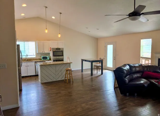 Vaulted ceiling, recessed lighting, wood-finish flooring, white cabinetry, and a ceiling fan