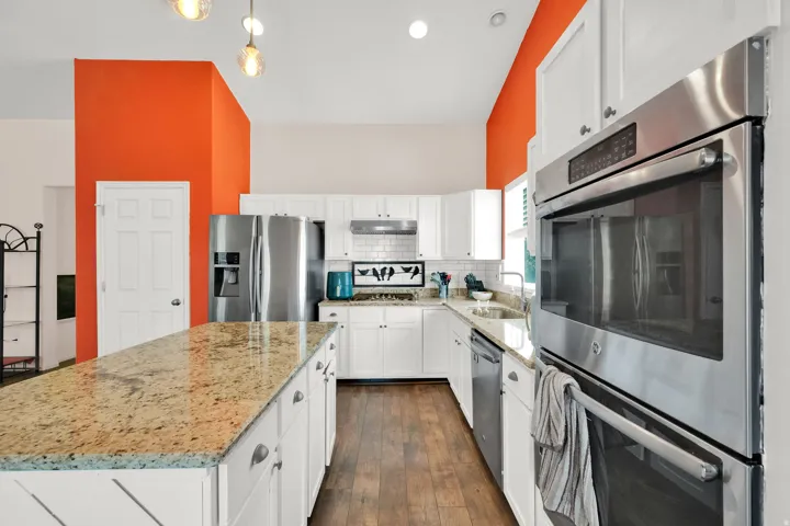 Kitchen featuring a granite-topped island, stainless steel double wall ovens, white cabinetry, wood-finish flooring, and a subway tile backsplash