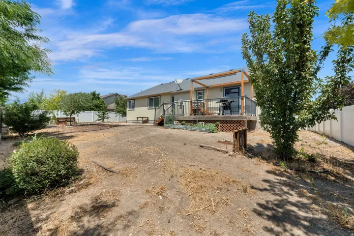 Expansive backyard featuring a raised deck with a wooden pergola, mature trees, and privacy fencing
