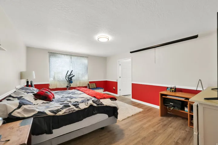 Bedroom featuring wood-finish flooring, a window with blinds, and two-tone wall treatment with a chair rail