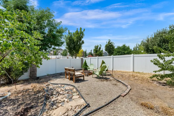 Gravel patio area featuring a white privacy fence, mature trees, and a brick border
