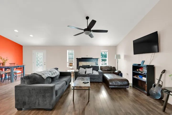 Spacious living area featuring wood-finish flooring, a ceiling fan with integrated lighting, and a bright accent wall