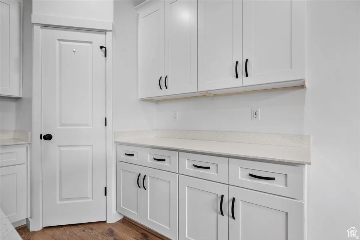 White cabinetry with black hardware, light-toned countertops, wood-finish flooring, and a paneled interior door