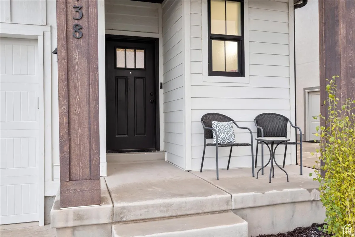 Inviting front entrance featuring a dark paneled door with glass inserts, white horizontal siding, a substantial wood-finish structural column, and a concrete porch