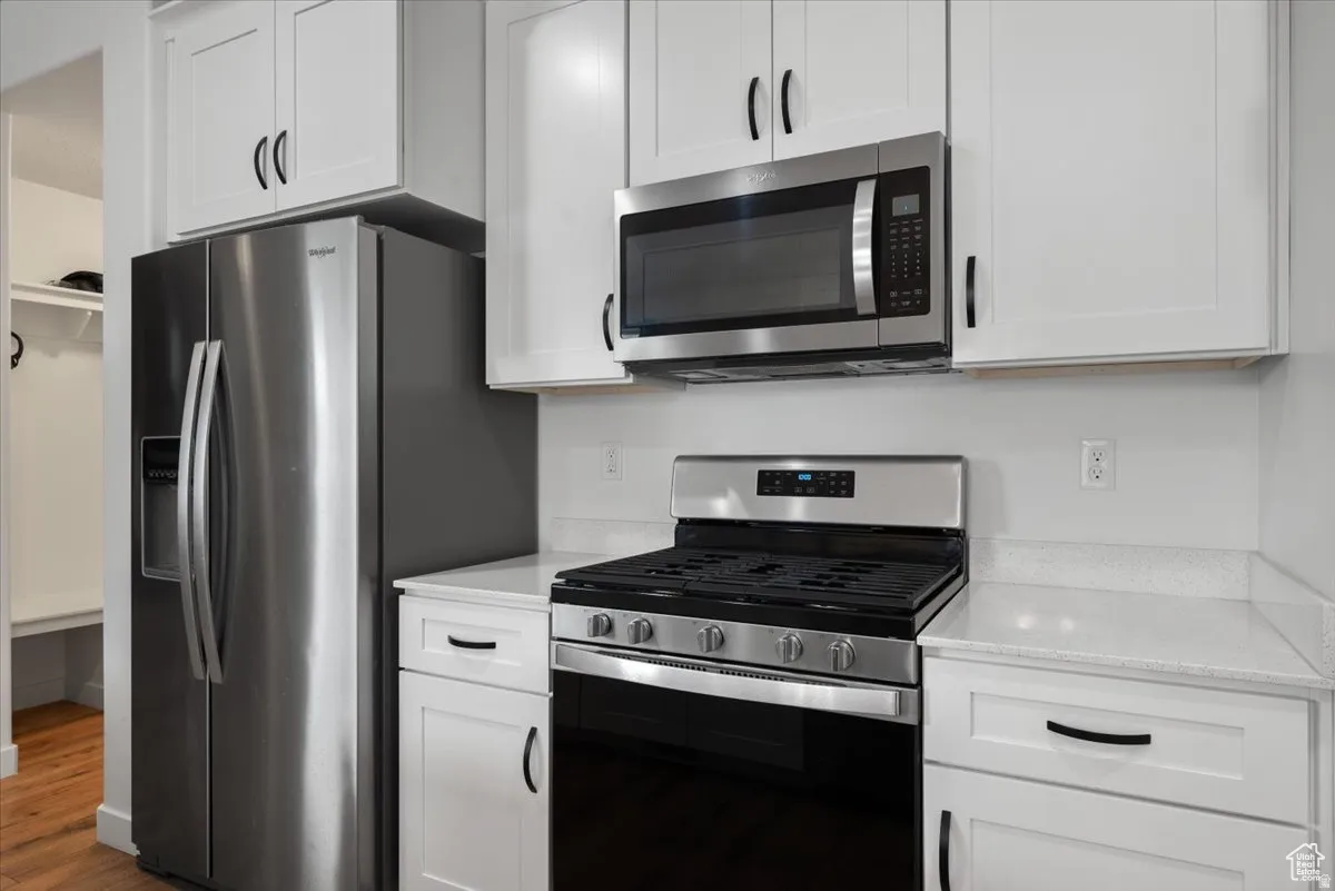Modern kitchen featuring stainless steel appliances, white shaker cabinetry, black hardware, an over-range microwave, and light-toned countertops