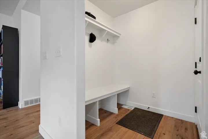 Entryway featuring wood-finish flooring, white walls, and a built-in bench with an overhead shelf and hooks