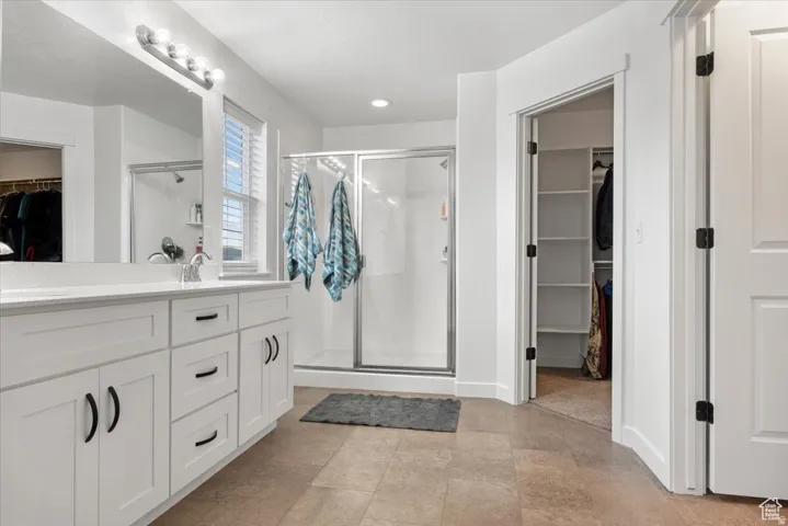 Bathroom featuring a white vanity with black hardware, a frameless shower, and light-colored tile flooring