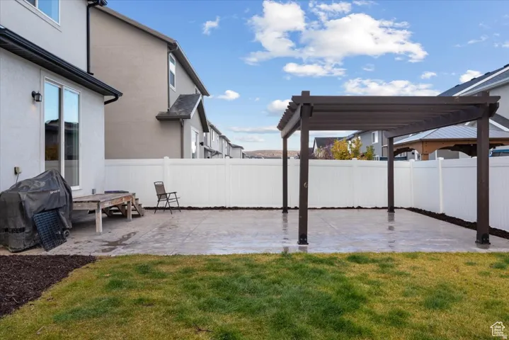 Private backyard featuring a dark wood-finish pergola, a large concrete patio, and a manicured lawn