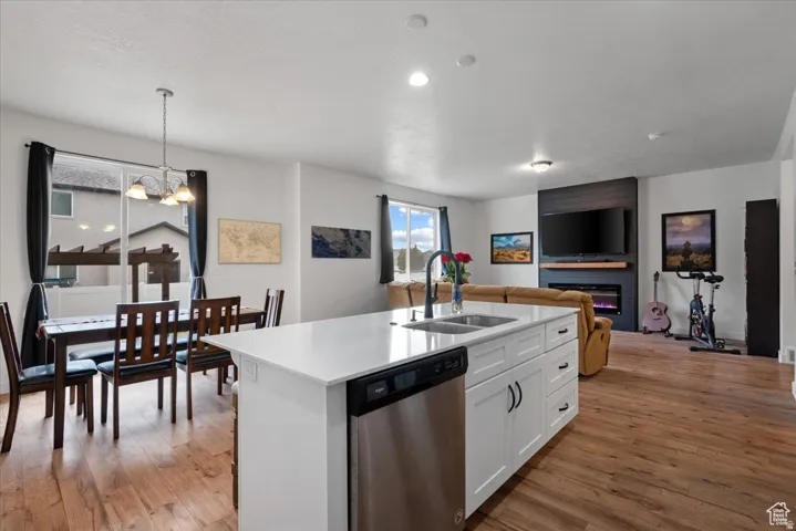 Open-concept living space featuring wood-finish flooring, a kitchen island with a stainless steel dishwasher, an integrated kitchen sink with a matte black faucet, and a fireplace with a dark wood surround