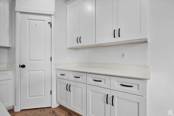 White cabinetry with black hardware, light-toned countertops, wood-finish flooring, and a paneled interior door