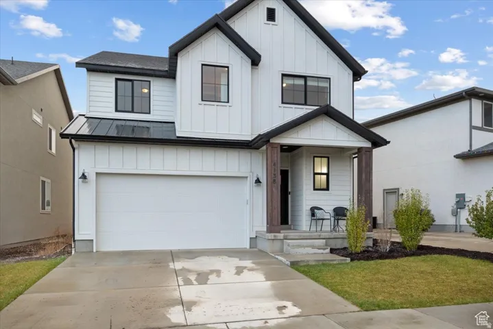 Modern farmhouse exterior featuring white vertical and horizontal siding, a black metal roof accent, dark-framed windows, a covered entry with wood-finish columns, and an integrated two-car garage
