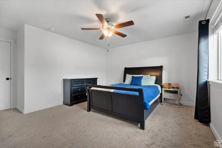 Carpeted bedroom with a ceiling fan, white walls, and a window with blinds