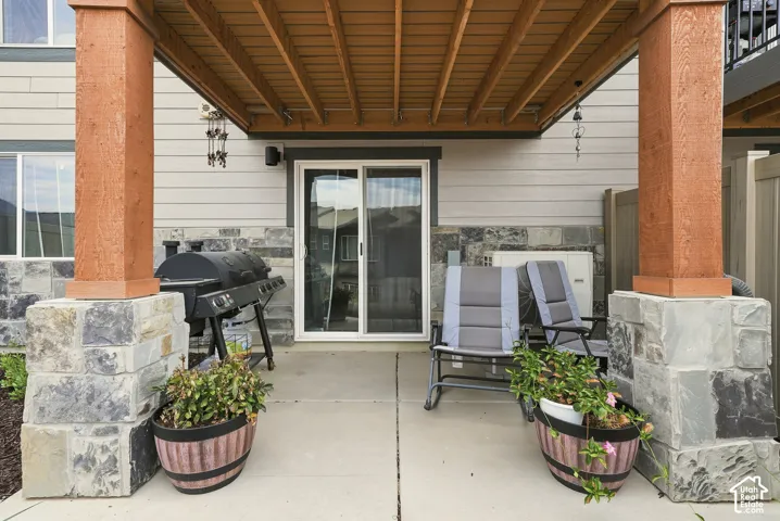 Covered patio featuring concrete flooring, stone-clad pillars, a wood-finish ceiling, and a sliding glass door