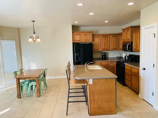Kitchen featuring wood cabinetry, black appliances, recessed lighting, and a center island with a sink