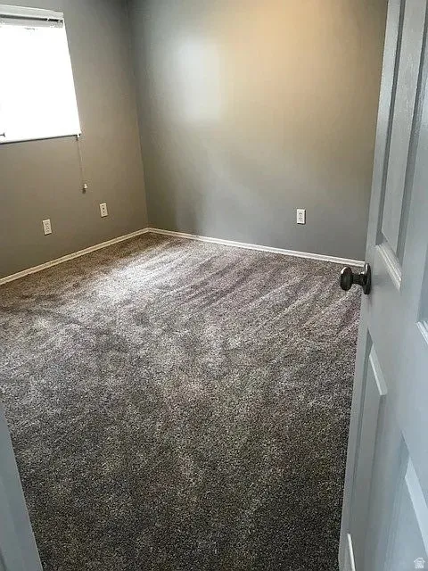 Carpeted basement bedroom featuring neutral wall paint, white baseboards, and a window with blinds