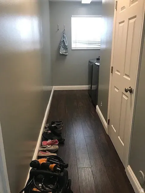 Laundry room featuring dark wood-finish flooring, light gray walls, a window with blinds, and a paneled interior door
