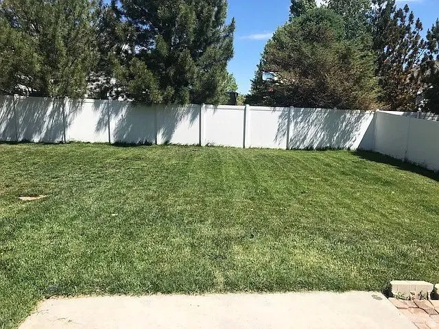 Expansive backyard featuring a manicured lawn, a full-height white privacy fence, and mature perimeter trees