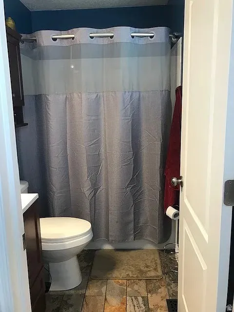 Bathroom with shower, featuring a white toilet, dark wood-finish cabinet with white countertop, and varied-tone tile flooring