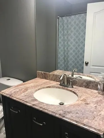 Master Bathroom vanity featuring a built-in oval sink, a patterned countertop, a wall-mounted mirror, and dark cabinetry with brushed nickel hardware