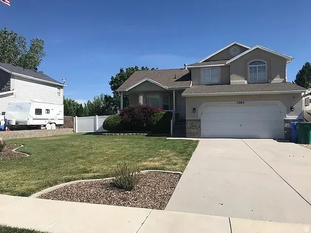 Two-story residence featuring a two-car garage, concrete driveway, and a front lawn with landscaped beds