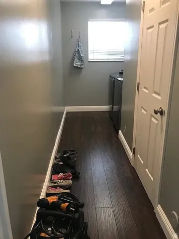 Laundry room featuring dark wood-finish flooring, light gray walls, a window with blinds, and a paneled interior door