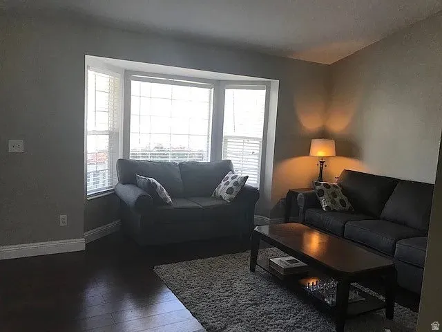 Living area featuring a bay window with natural light, dark wood-finish flooring, and light-toned wall finishes