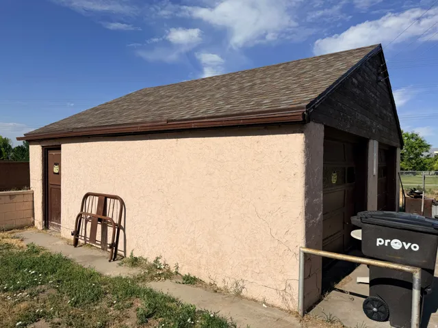 Detached structure featuring stucco exterior, asphalt shingle roofing, and brown rain gutters